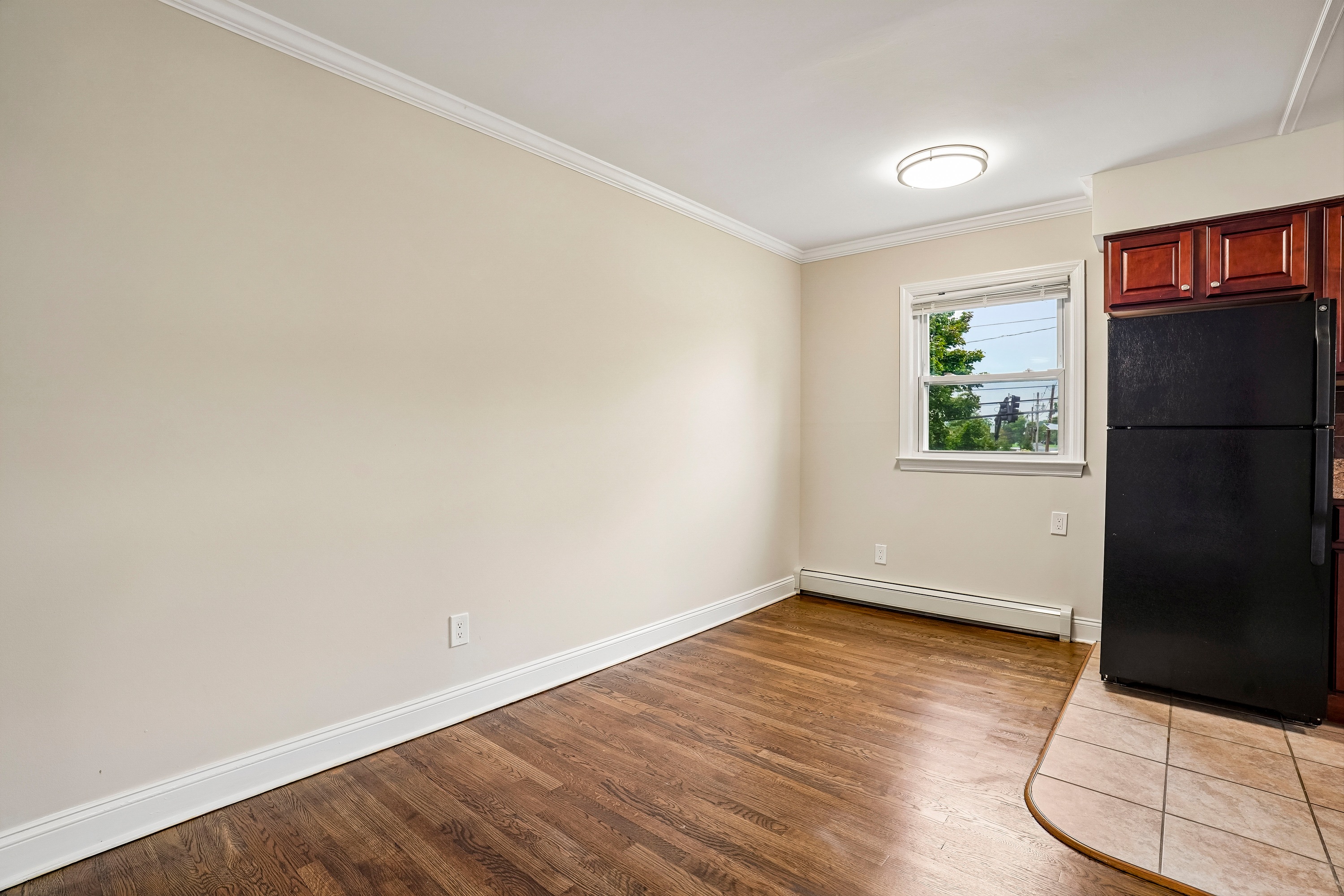 A room with a black fridge and wooden flooring.